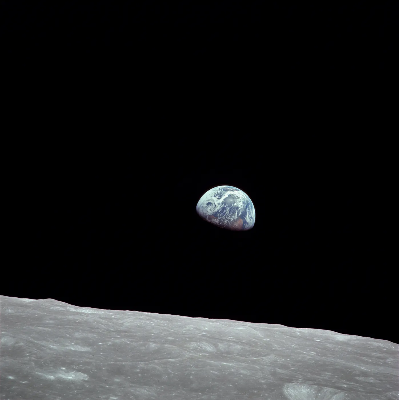 The Earth, half lit, rising above the grey, cratered horizon of the Moon against black space