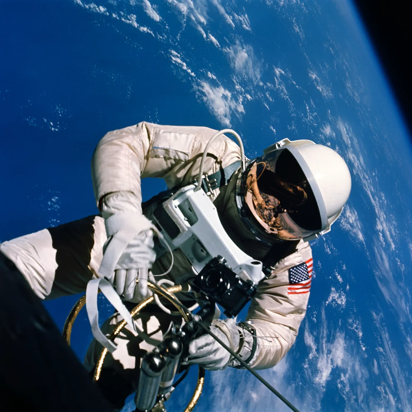 An astronaut in a white spacesuit floats above the blue Earth, tethered to his spacecraft