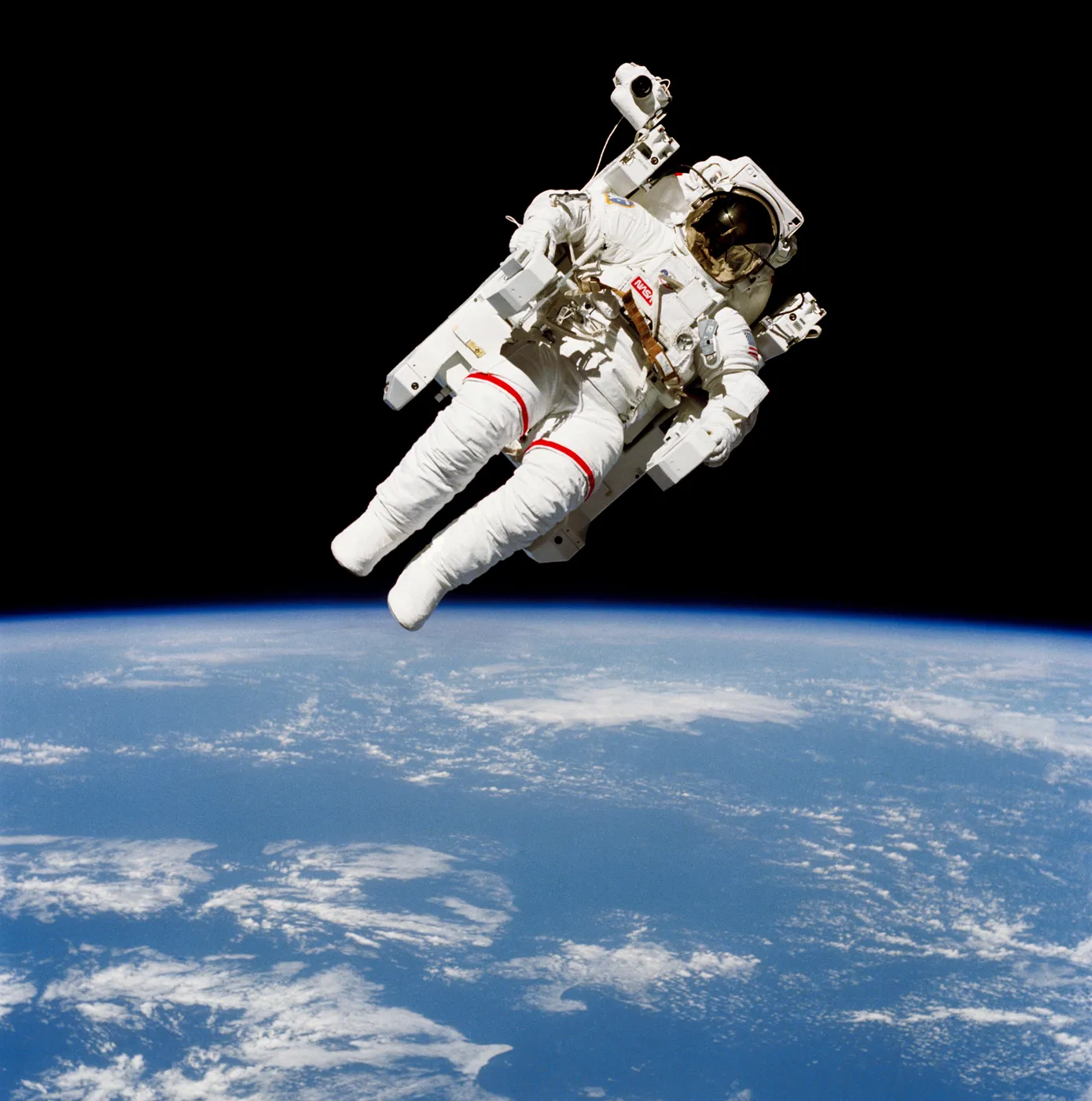 An astronaut in a jet backpack floats free in black space above the blue Earth